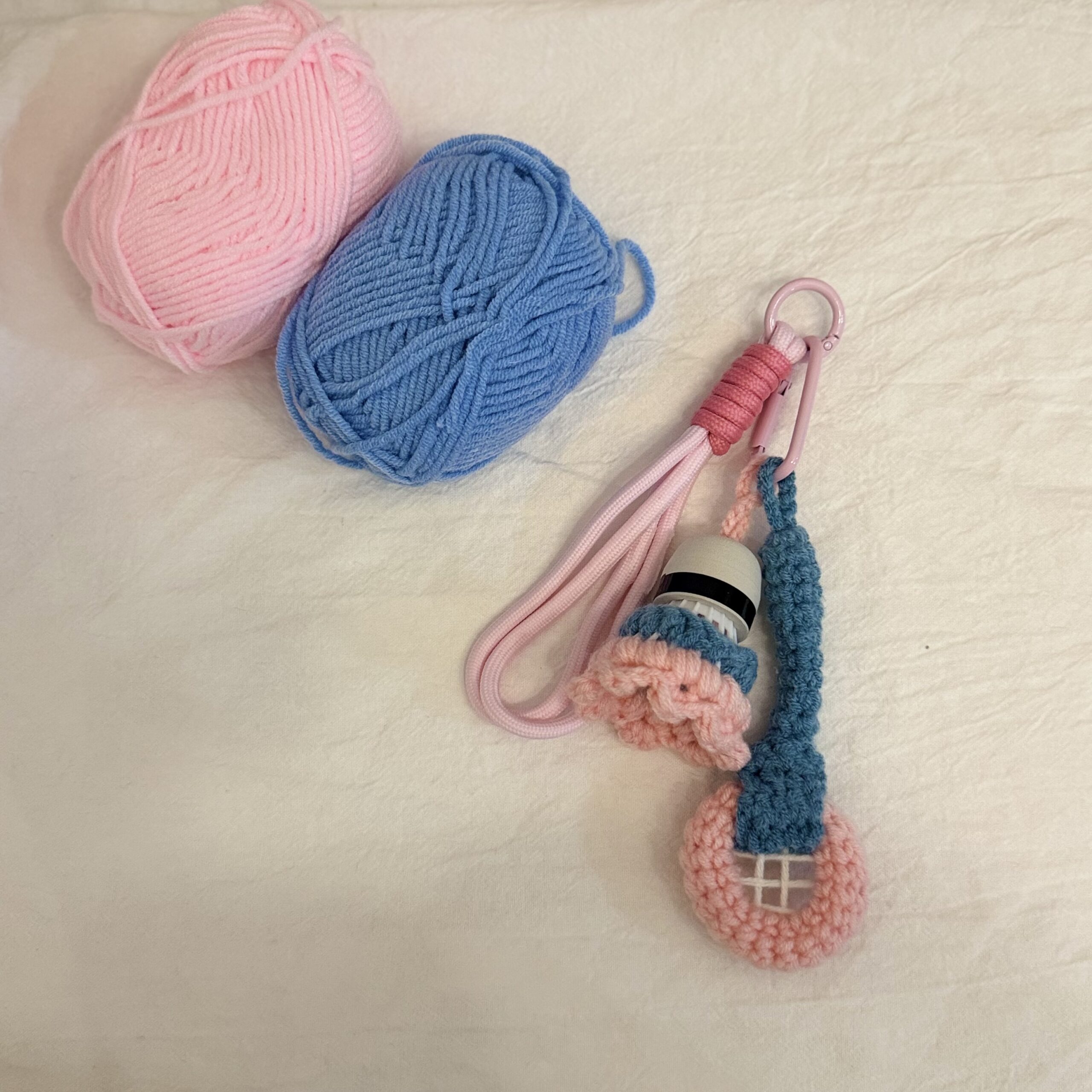 Badminton-Anhänger neben rosa und blauem Garn, mit rosa Schlaufe, blauem Schlägerdetail und gehäkelten rosa Akzenten.