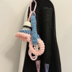 Seitliche Ansicht des rosa-blauen Badminton-Anhängers an einer schwarzen Netztasche, mit sichtbarem Federball und Garnstruktur.