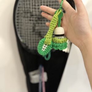 Handgemachter grüner Badminton-Anhänger vor einer Sporttasche, mit Federball, Schlägerform und grünem Metallclip.