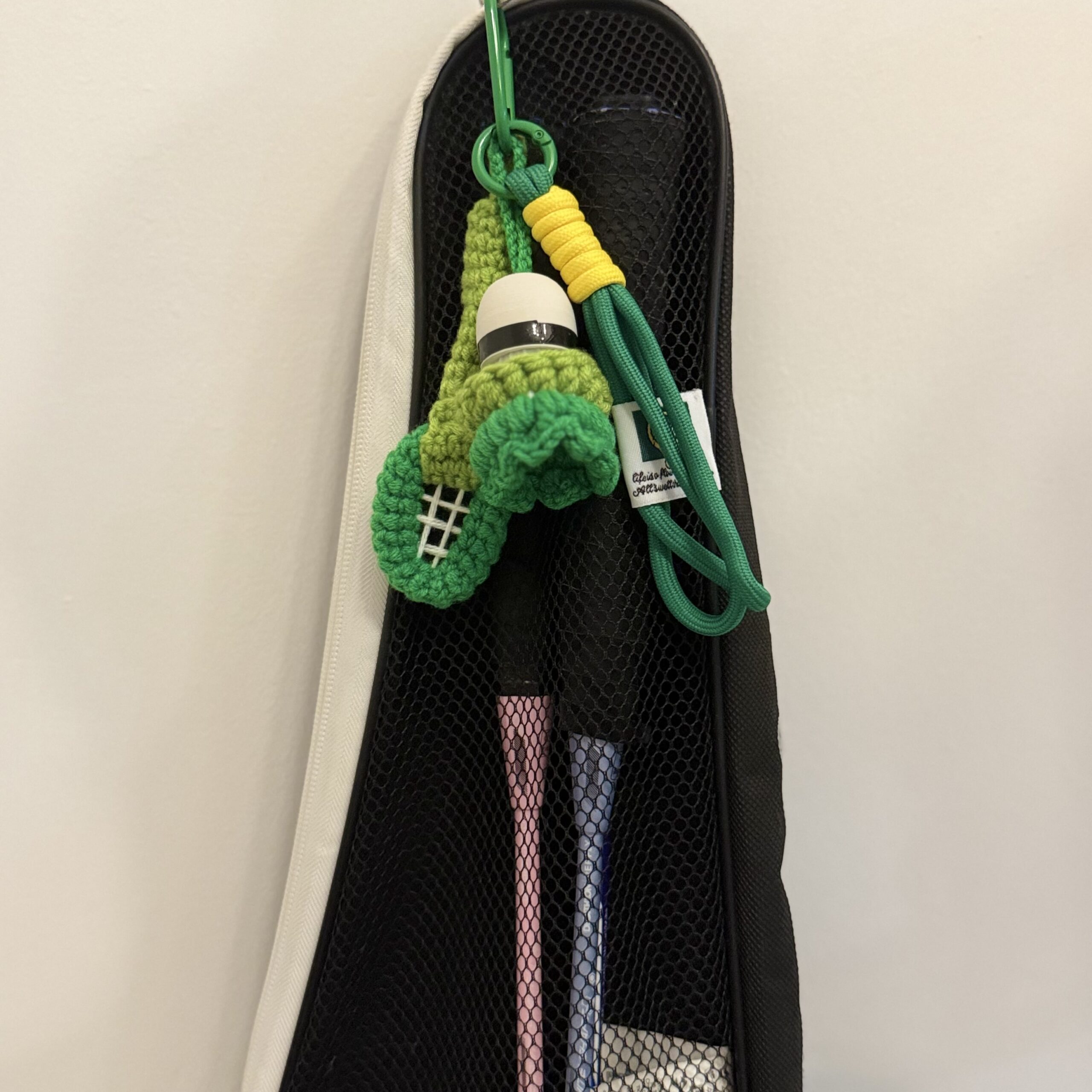 Grüner Federball-Schlüsselanhänger an einer Badmintontasche befestigt, mit Schläger-Motiv, Kordel und gelbem Wickeldetail.