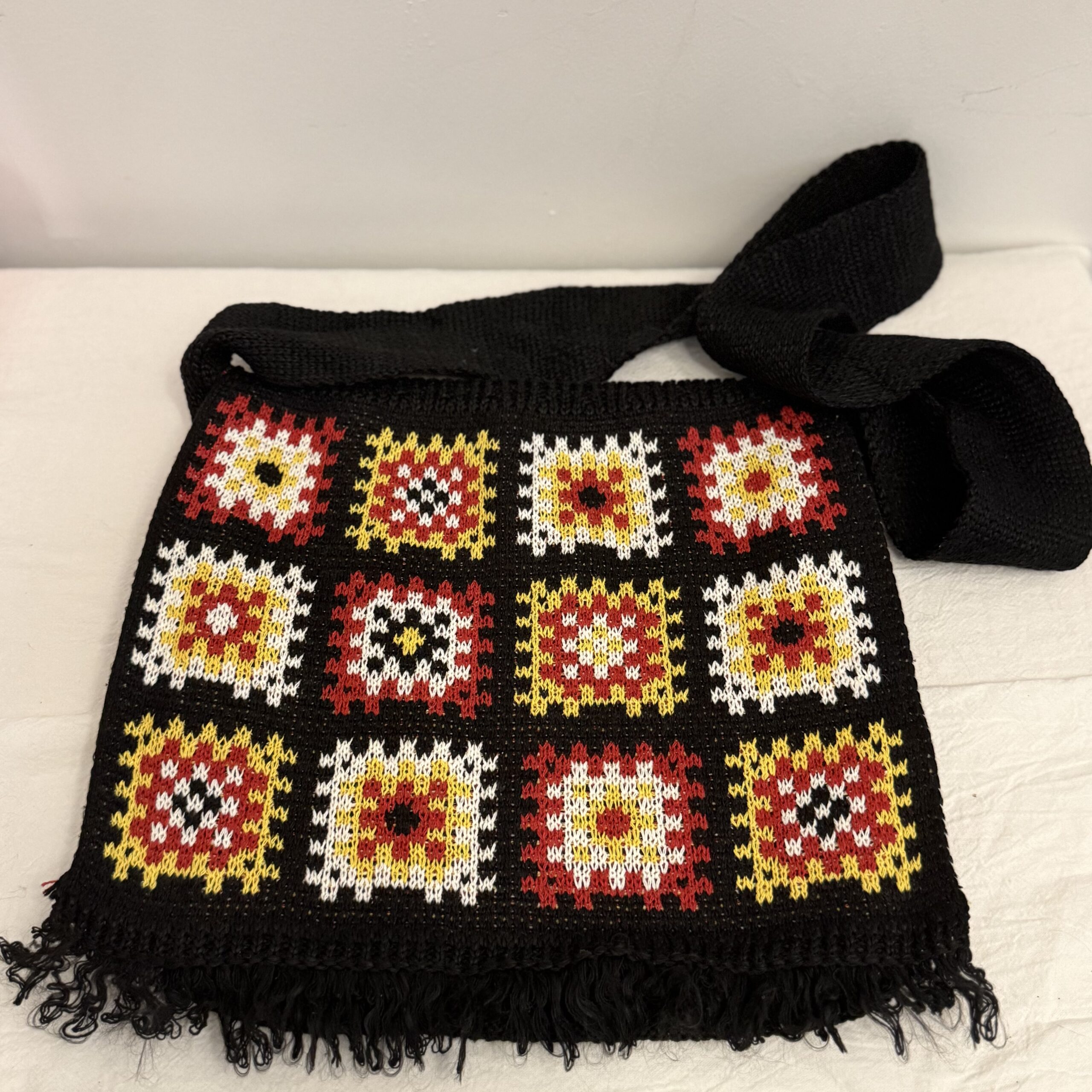 Schwarze handgemachte Stricktasche mit rotem, gelbem und weißem Granny-Square-Muster, breitem Träger und Fransen