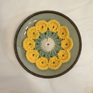 Draufsicht auf einen floralen Garn-Untersetzer mit gelben Bluetenblaettern in einer gruenlichen Schale