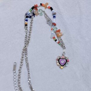 Bunte Perlenkette mit silberfarbener Kette, Candy-Perlen, transparenten Schmuckelementen und violettem Herz Anhänger auf hellem Stoff