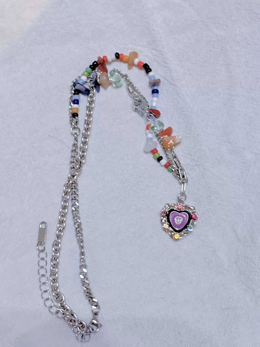 Bunte Perlenkette mit silberfarbener Kette, Candy-Perlen, transparenten Schmuckelementen und violettem Herz Anhänger auf hellem Stoff
