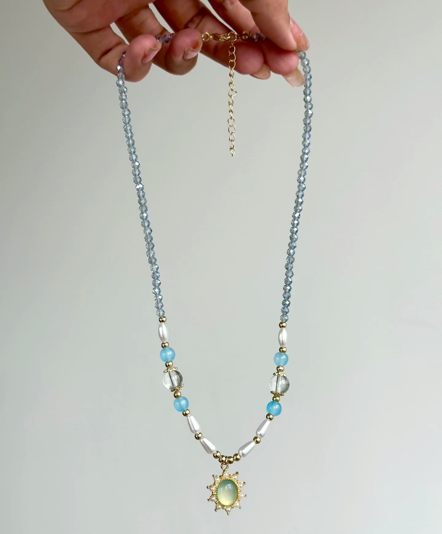 Lange Ansicht der hellblauen Perlenkette mit goldfarbenem Verschluss und Verlängerungskette.