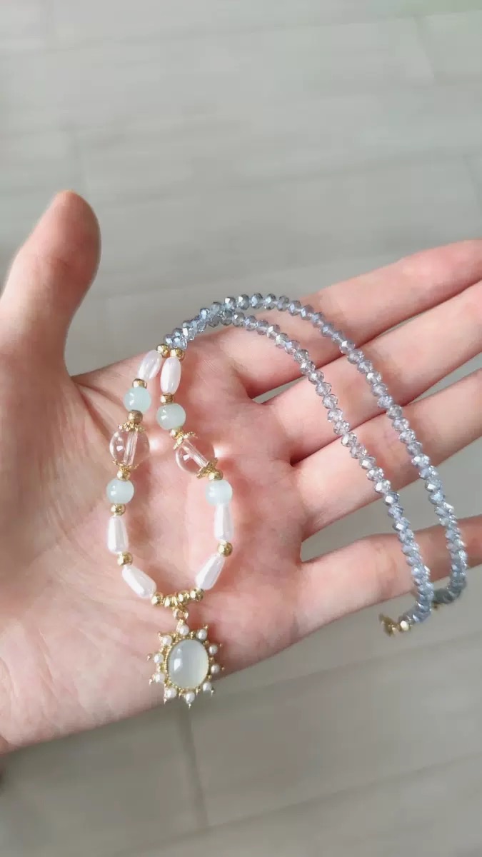 Hellblaue Perlenkette mit transparenten Facettenperlen und Sonnenanhänger in einer Hand gehalten.