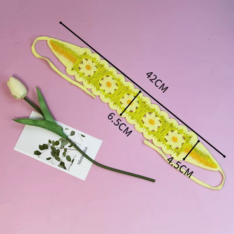 Grün-gelbes Strick-Haarband mit Gänseblümchen-Muster und Maßangaben 42 cm, 6,5 cm und 4,5 cm auf rosa Hintergrund.