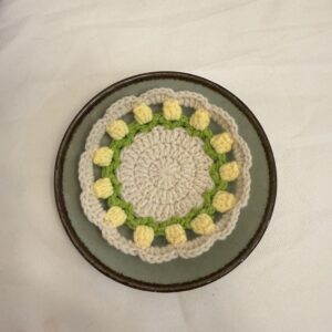 Gelber Tulpen-Tassenuntersetzer auf einem Teller, fotografiert von oben mit sichtbarer runder Form und floraler Struktur.
