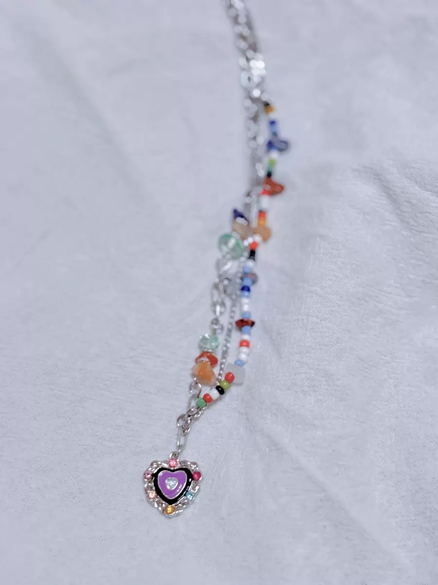 Nahaufnahme einer bunten Perlenkette mit violettem Herz Anhänger, silberfarbener Kette und Candy-Farben auf hellem Hintergrund